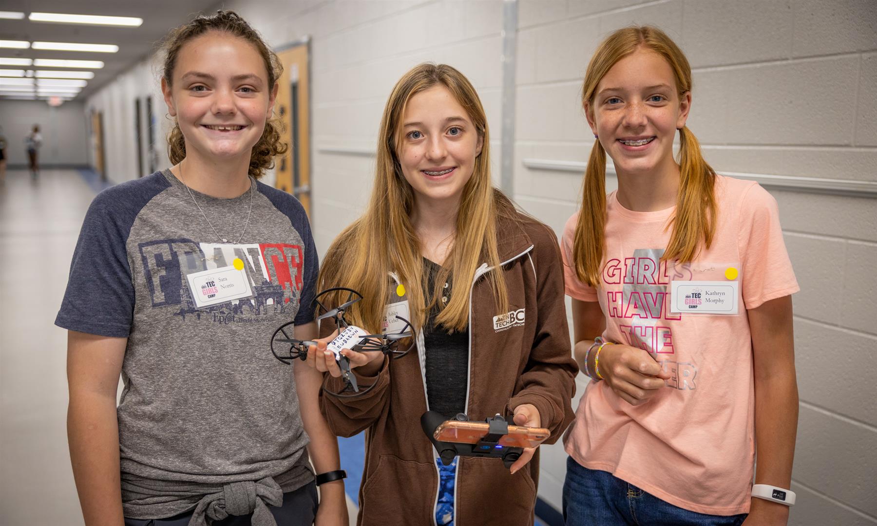 Three girls smile while holding a drone and controller